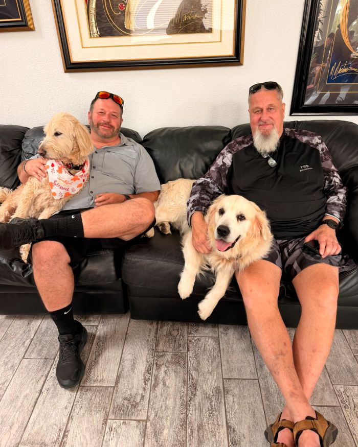 Jerry y un amigo en un sillón con Astro, el goldendoodle, y Tex, el golden retriever inglés